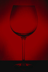 large glass, empty red wine glass on a red background with reflection and highlights on the edges