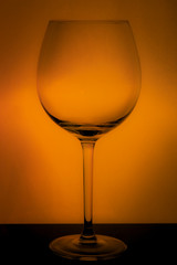 large glass, empty red wine glass on a yellow background with reflection and highlights on the edges