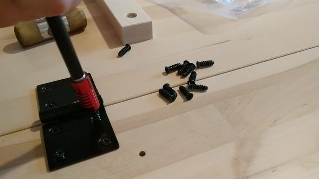 Fixing with a black metal hinge on two light wooden boards. The screwdriver is used for screwing. 25Fps