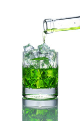 on a white background with a reflection is a glass glass glass filled with ice, it flows from a glass bottle of green lemonade (drink)