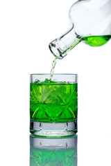 on a white background with a reflection is a glass glass glass filled with ice, it flows from a glass bottle of green lemonade (drink)
