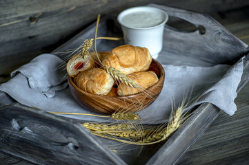 Croissants, a cup with kefir and ears of grain on a wooden tray. The concept of a wholesome breakfast.