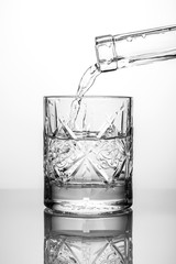 Crystal glass with water and bottle neck on white background with reflection