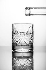 Crystal glass with water and bottle neck on white background with reflection
