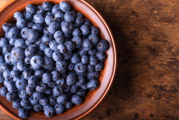 Tasty ripe blueberries in a clay bowl on a rustic wooden table close-up, copy space