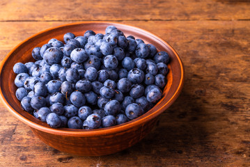 Tasty ripe blueberries in a clay bowl on a rustic wooden table close-up, copy space