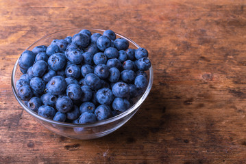 Tasty ripe blueberry berries in a glass cup on a rustic wooden table close-up