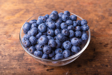 Tasty ripe blueberry berries in a glass cup on a rustic wooden table close-up