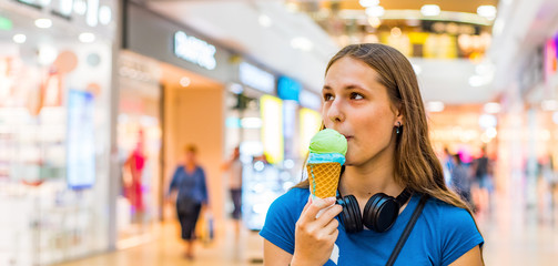 portrait of young teenager brunette girl with long hair eating tasty cone ice cream in shopping mall