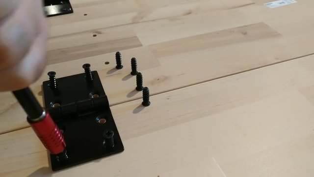 Fixing with a black metal hinge on two light wooden boards. The screwdriver is used for screwing. 30Fps