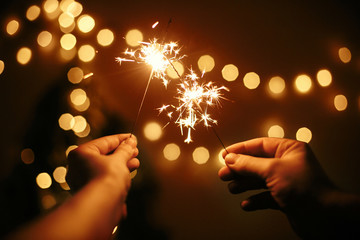 Glowing sparklers in hands on background of golden christmas tree lights, couple celebrating in...