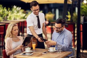 Happy waiter giving the menu to a couple in a cafe.