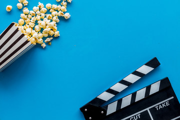 Watch film in cinema with popcorn and clapperboard on blue background top view