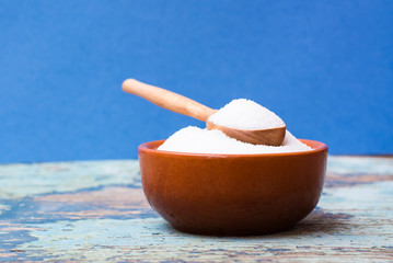 Sugar in a bowl and in a wooden spoon on a wooden table