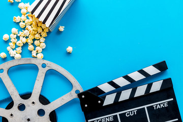 Watch film in cinema with popcorn, video tape and clapperboard on blue background top view