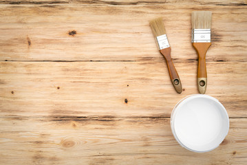 Paint brushes and a can with white paint on a wooden textured flat lay background with a copy space.