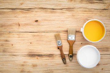 Paint brushes and a cans with yellow and white paint on a wooden textured flat lay background with a copy space.