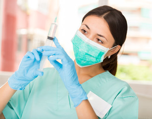 Girl nurse in mask holding syringe for injection in clinic