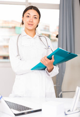 Girl doctor in white medical coat holding clipboard in office