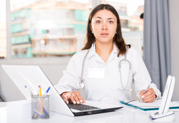 Attentively female doctor  working at laptop and writing papers