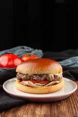 Classic american burger with juicy beef patty, glossy bun, cheddar cheese and vegetables on a minimalistic black background