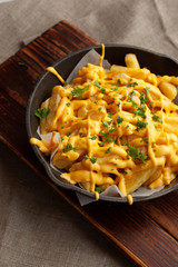 Mouthwatering hot french fries with a lot of cheese sauce with herbs in a pan, on a wooden board