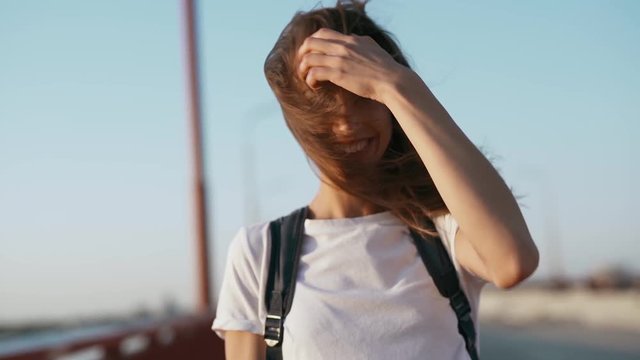happy joyful smiling young pretty woman in white t-shirt is standing on the bridge on blue sky background, laughing, enjoying peaceful sunset and looking at camera. slow motion Full HD stock footage