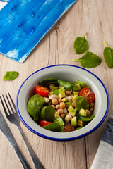 Dietary summer salad with little spinach leaves, beans, chickpea and tomato on a light wooden background with ingredients