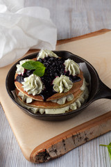 Stack of fluffy pancakes with whipped cream and blueberry sauce, powder with green matcha and...