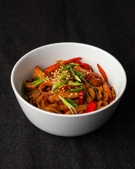 Wheat thick wok noodle with roasted bell pepper, soy sauce, chicken, carrot and sesame on black background