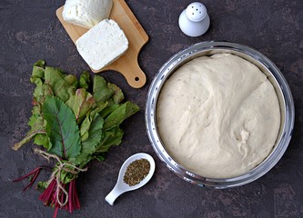 Cooking Ossetian pies with beet tops and cheese, step one. Ready yeast dough, white Suluguni cheese, fresh beet tops, spices, salt. Caucasian cuisine. Top view.