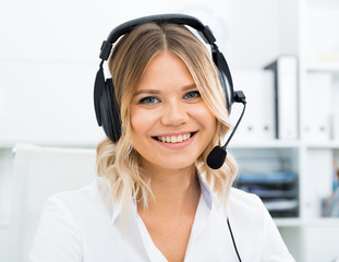 Young call center employee in headphones is sitting near laptop in the office