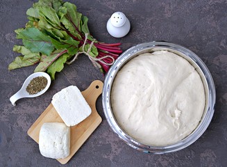 Cooking Ossetian pies with beet tops and cheese, step one. Ready yeast dough, white Suluguni cheese, fresh beet tops, spices, salt. Caucasian cuisine. Top view.