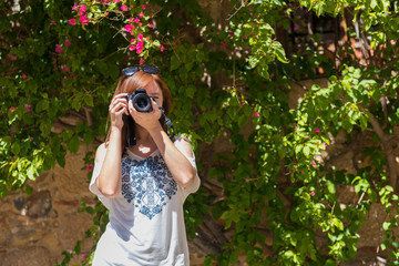 A young woman with reddish hair takes photographs with her camera next to a wall covered with...