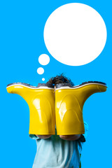 a boy in a light t-shirt covered his face with yellow rubber boots. symbolizes autumn on blue background