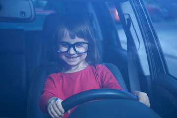 Driving shool. Humorous portrait of cute little child girl learns to drive. Horizontal photo.
