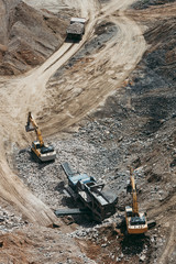 Heavy machinery excavators working on quarry and loading stone and granite into dump trucks. Bird eye perspective photo.