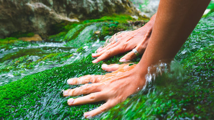 Tanned female hands stroke green moss growing in the clear and transparent water of a mountain...