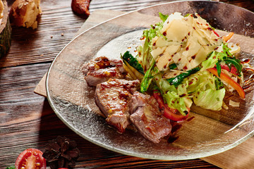 Roasted meat slices and Salad with fresh vegetables and parmesan in transparent plate on wooden background in beautiful composition among vegetables and spices. Top view. Flat lay