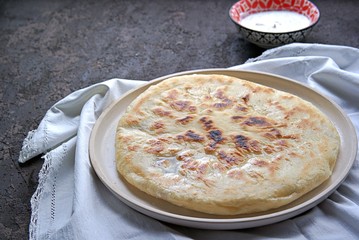 Ossetian pie with beet tops and cheese on a white clay plate. Served with sour cream, garlic and greens sauce. Caucasian cuisine.