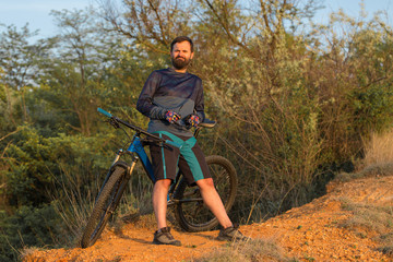 Naklejka premium Cyclist in shorts and jersey on a modern carbon hardtail bike with an air suspension fork rides off-road on the orange-red hills at sunset evening in summer 