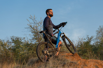 Obraz premium Cyclist in shorts and jersey on a modern carbon hardtail bike with an air suspension fork rides off-road on the orange-red hills at sunset evening in summer 