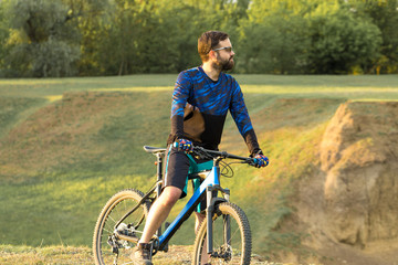 Naklejka premium Cyclist in shorts and jersey on a modern carbon hardtail bike with an air suspension fork rides off-road on the orange-red hills at sunset evening in summer 