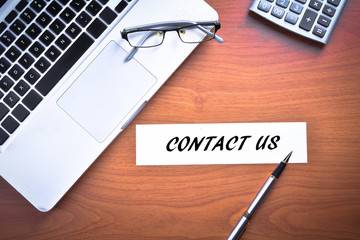 Laptop with glasses, pen and calculator with text CONTACT US