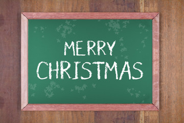 Chalkboard with christmas decoration on a wooden background and text "Merry Christmas", written on it