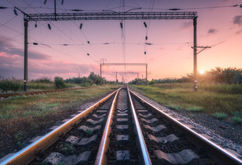 Railroad and pink sky at sunset. Summer rural industrial landscape with railway station, sky with colorful clouds and sunlight, green grass. Beautiful railway platform. Freight transportation. Cargo