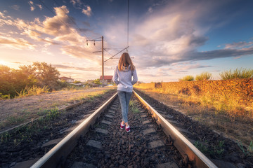 Standing young woman on the railroad at sunset in summer. Slim girl on the railway station. Rural...
