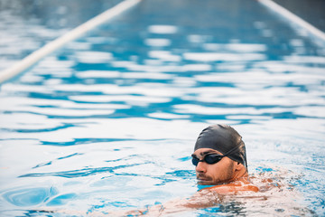 Fototapeta na wymiar back view of muscular swimmer in swimming cap and goggles standing at swimming pool