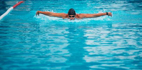 Professional man swimming in butterfly style with hat and goggles at the pool