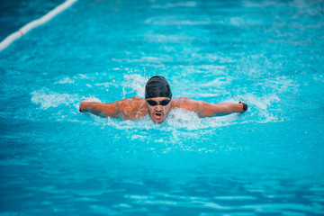 Professional man swimming in butterfly style with hat and goggles at the pool
